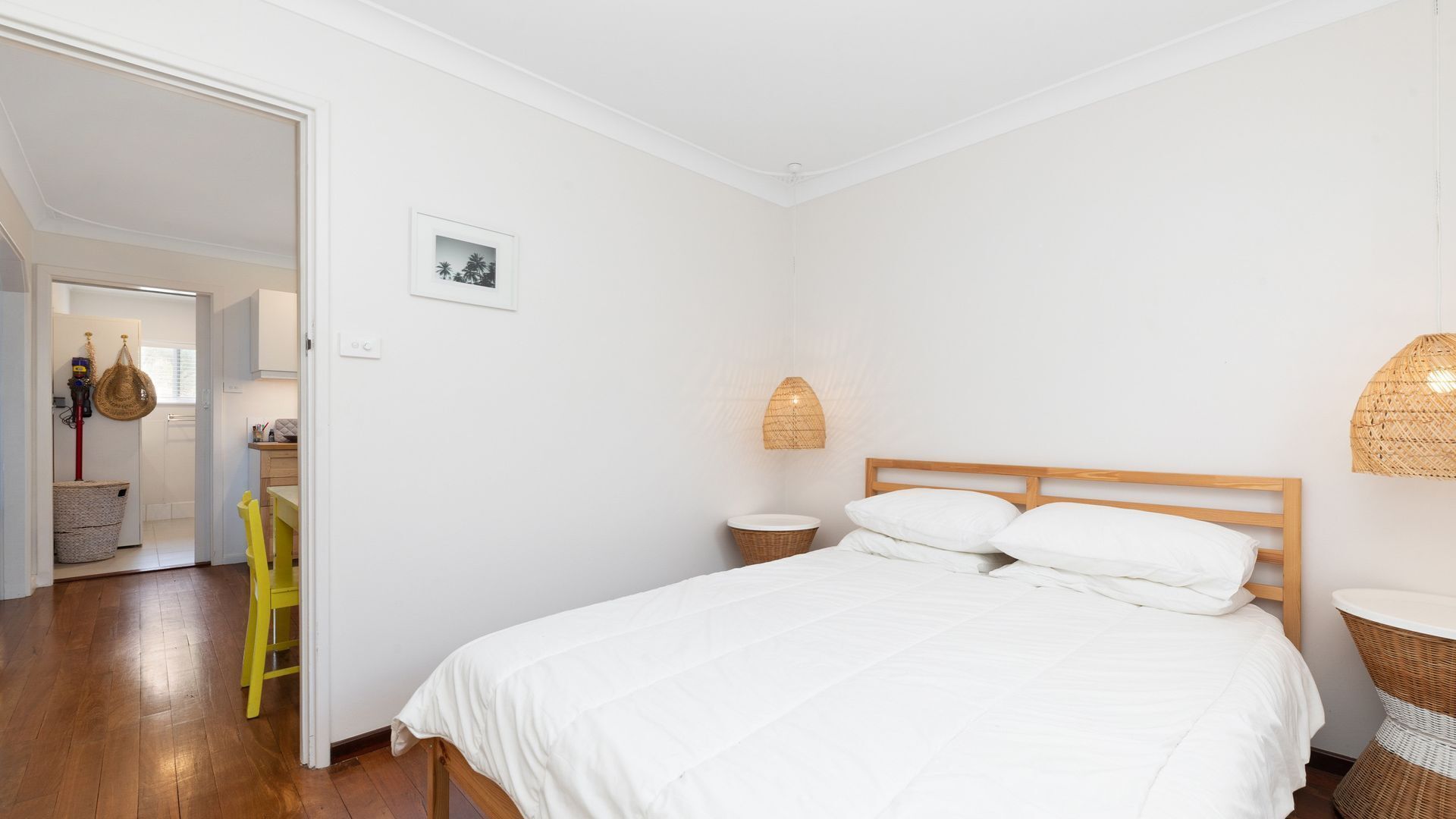 A bedroom with a wooden bed, a small bedside table, a wicker chair, and a wicker basket.
