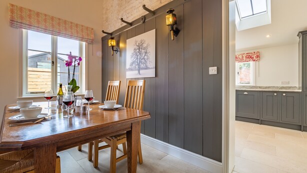 A dining area with a wooden table set for four, two wall-mounted lights, and a painting of a tree.