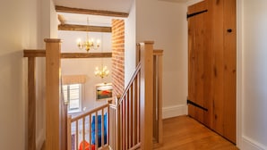 A wooden staircase with a chandelier, a brick wall, and a wooden door.
