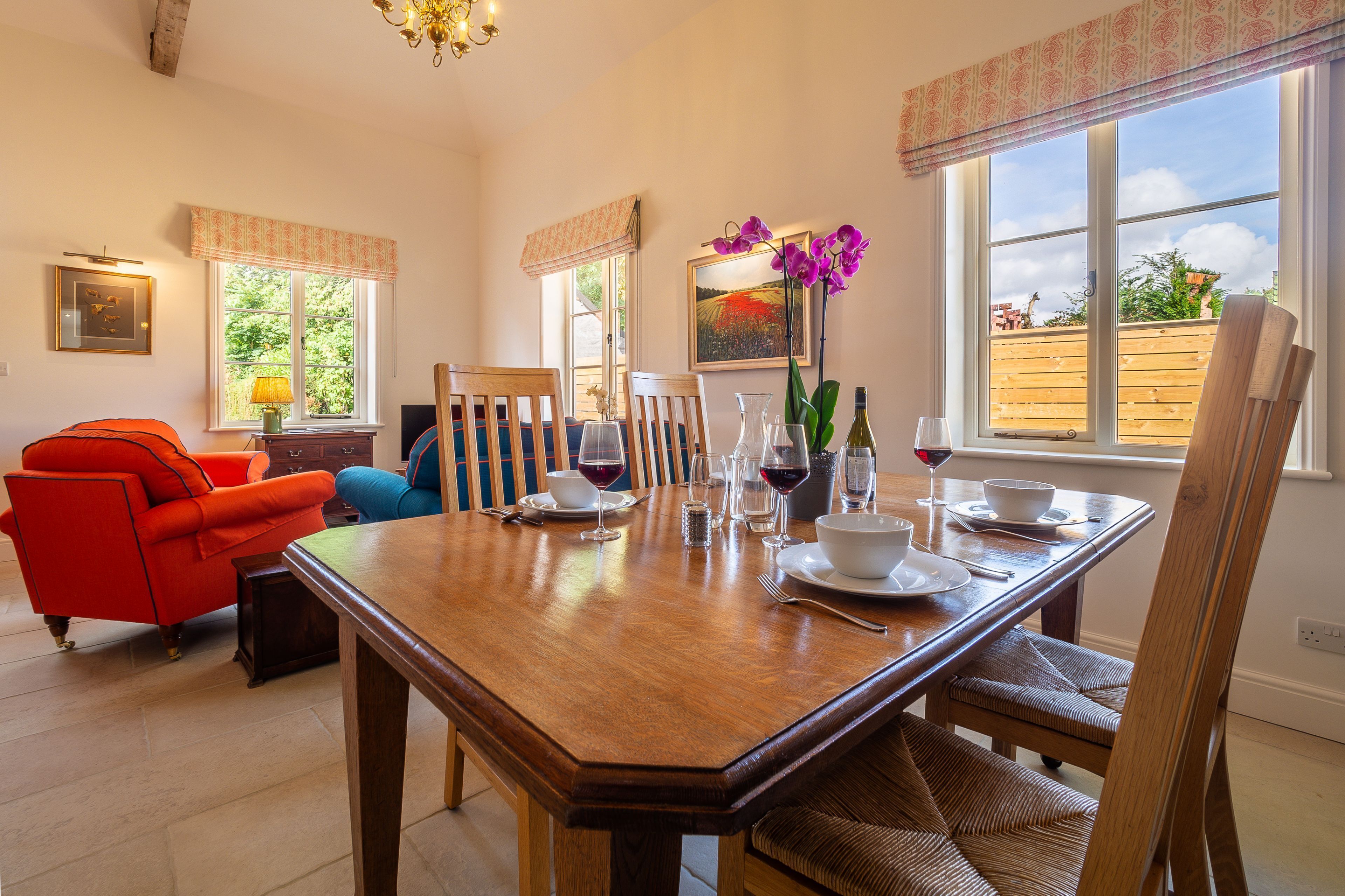 A dining area with a wooden table set for four, surrounded by chairs, a sofa, and a small side table.