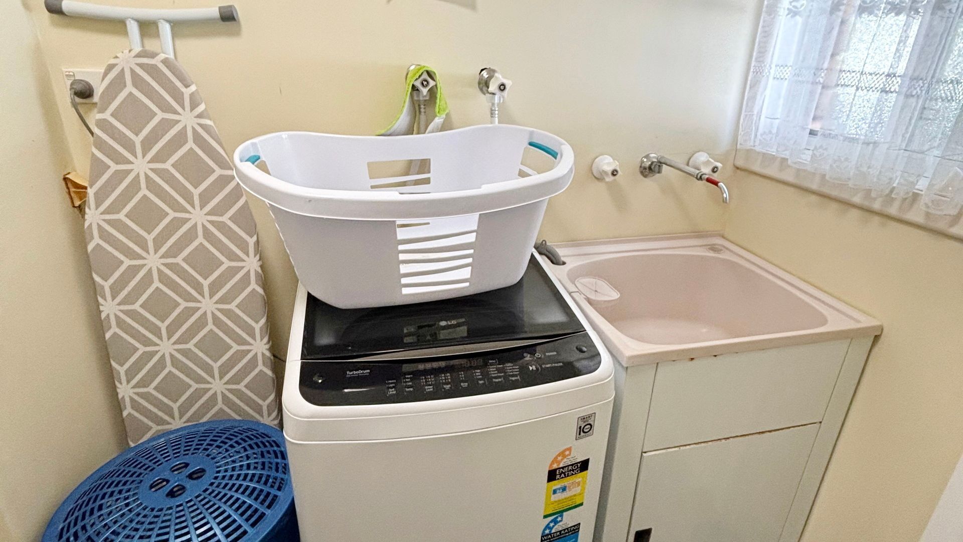 A compact laundry area with a washing machine, a drying rack, and a small sink.