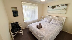 Une chambre à coucher avec un lit, une chaise, une fenêtre avec des rideaux, une table de chevet et un tableau au mur.