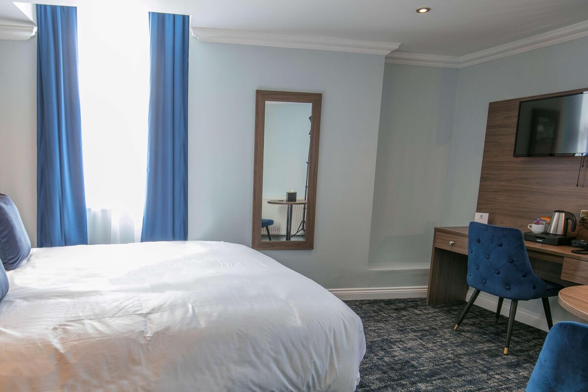 A hotel room with a large bed, a desk, a chair, a TV, and a mirror.