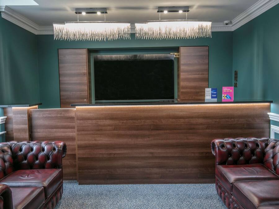 Een receptiegedeelte met een houten balie, twee leren banken, een grote flatscreen-tv en een sierlijke kroonluchter.