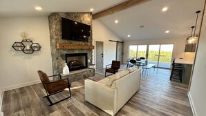 A spacious living area with a stone fireplace, a flat-screen TV, a sofa, and a dining area with a table and chairs. - Travelers Rest, Furman, Greenville, and a mountain view! (Travelers Rest)