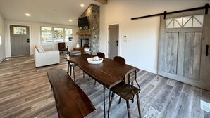 A spacious dining area with a wooden table and benches, a stone fireplace, and a large sliding barn door. - Travelers Rest, Furman, Greenville, and a mountain view! (Travelers Rest)