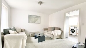 A spacious living room with a sofa, a coffee table, and a couch. There is a washing machine in the adjacent room. - Ammaculate 3 Bedroom Property Near Caltic Manor (Newport)