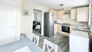 A compact kitchen with a refrigerator, microwave, stove, and sink. There is a dining area with a table and chairs. - Ammaculate 3 Bedroom Property Near Caltic Manor (Newport)