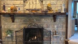 A stone fireplace with a mantel displaying model ships and a small statue. - Seneca Riverfront Spa! Hot tub, Pool + Sauna! Pontoon Boat and Canoe Available! (Baldwinsville)