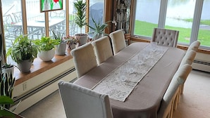 A dining area with a long table, chairs, and potted plants. - Seneca Riverfront Spa! Hot tub, Pool + Sauna! Pontoon Boat and Canoe Available! (Baldwinsville)