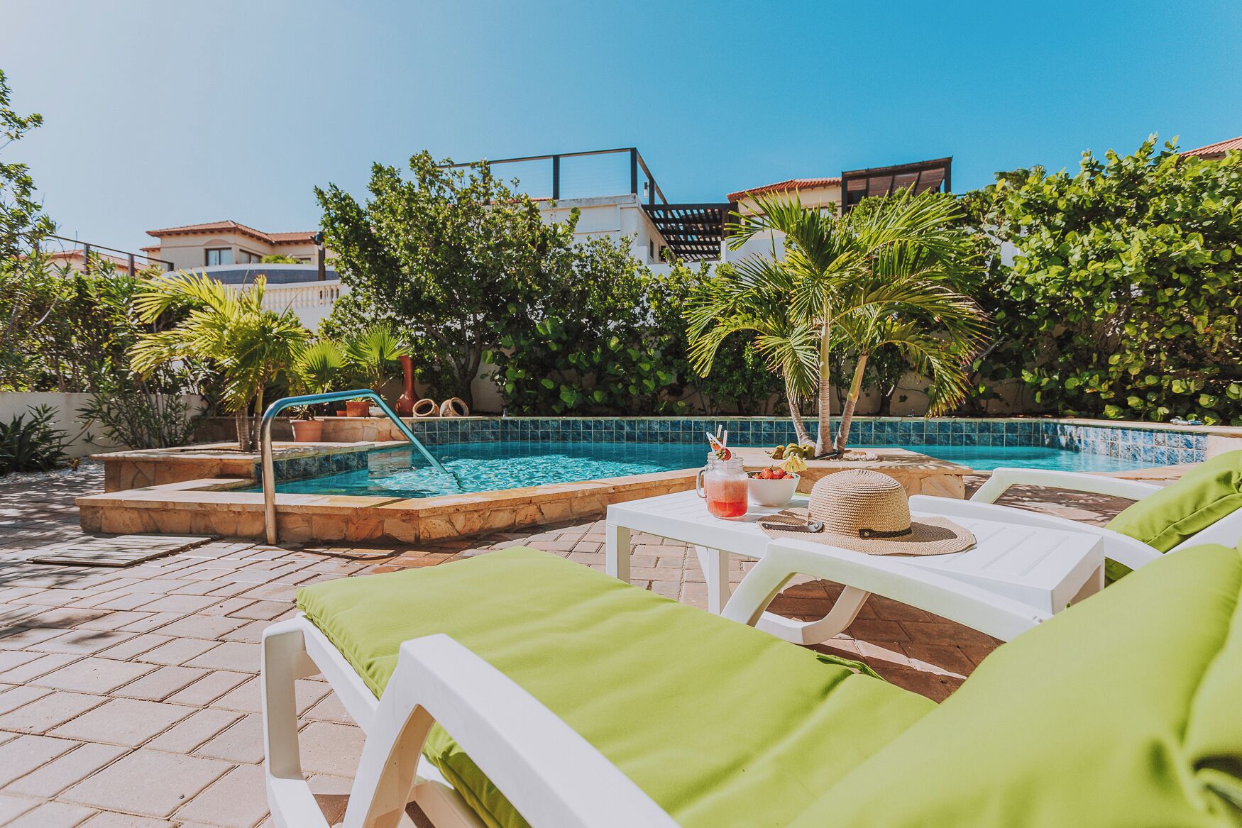A poolside area with a swimming pool, lounge chairs, and a table with drinks and a hat.