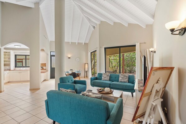 A spacious living area with teal sofas, a coffee table, and a painting on easel.