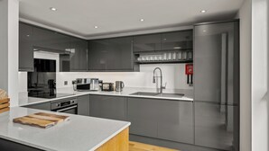 A modern kitchen with grey cabinets, a stainless steel refrigerator, and a wooden cutting board on the counter.