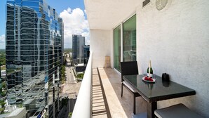 A balcony with a glass table, a bottle of champagne, and a chair. - Skyline City Views | Pool, Hot Tub & Fitness Room! (Miami)