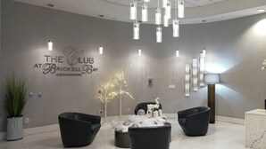A modern lobby with a chandelier, black seating, a plant, and a sign reading "The Club at Brickell Bay Condominium". - Skyline City Views | Pool, Hot Tub & Fitness Room! (Miami)