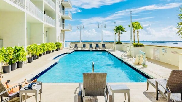 A pool area with lounge chairs and potted plants, overlooking a body of water. - Skyline City Views | Pool, Hot Tub & Fitness Room! (Miami)