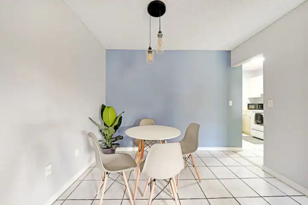 A dining area with a round table and four chairs, a potted plant, and a ceiling light fixture.
