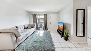 A modern living room with a sofa, a flat-screen TV, a potted plant, and a large mirror. - Fuseball & Games - 2 BD / 2 BTH Condo Miami! (Miami)
