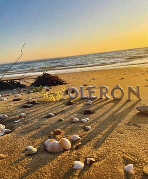 Uma praia com a palavra 'OLERON' escrita em grandes letras na areia, rodeada por conchas espalhadas.
