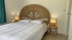 A bed with a woven headboard, two bedside tables with lamps, and a teal curtain. - Family home for up to 10 people, 15 min walk from the beach (Dolus-d'Oléron)