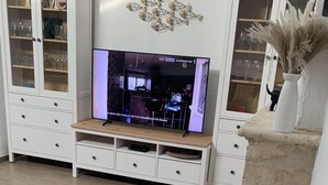 A living room with a television, white cabinets, and a wicker chair with a lamp. - Family home for up to 10 people, 15 min walk from the beach (Dolus-d'Oléron)