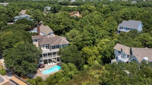 Vista aerea di una zona residenziale con case circondate da alberi rigogliosi, una piscina e vista sull'oceano.