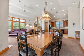A spacious living area with a large wooden dining table, leather sofa, and a staircase leading to another level.