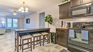 A modern kitchen with a central island, bar stools, a microwave, oven, and a ceiling fan.