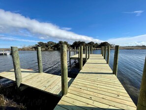 Une jetée en bois s’étendant sur une étendue d’eau calme, entourée d’arbres et sous un ciel dégagé.