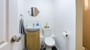 Pieni, siisti kylpyhuone, jossa on valkoinen pesuallas, wc-istuin ja peili pesualtaan yläpuolella.