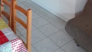 A compact kitchen with white cabinets, a black countertop, and a sink. There is a clock on the wall and a chair with a checkered tablecloth.