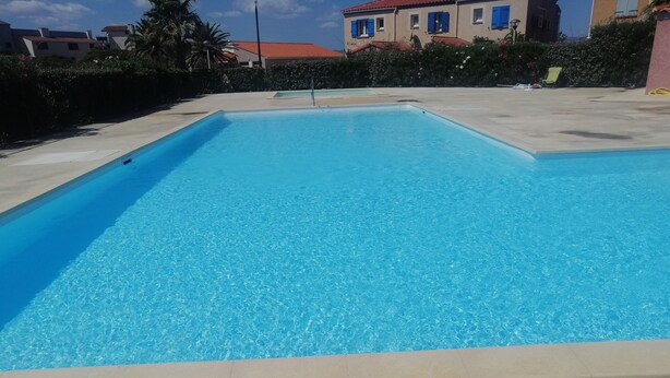 A rectangular swimming pool with clear blue water, surrounded by a concrete deck.