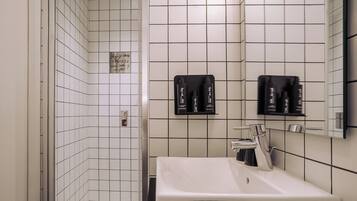 A modern bathroom with white tiled walls, a white sink, and two black toiletry dispensers mounted on the wall.
