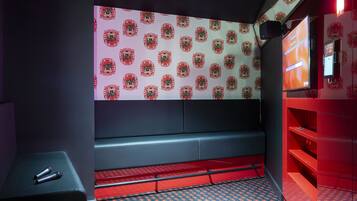 Une pièce avec un mur orné de motifs, un banc, une petite table avec un microphone et un tapis aux motifs rouges et bleus.