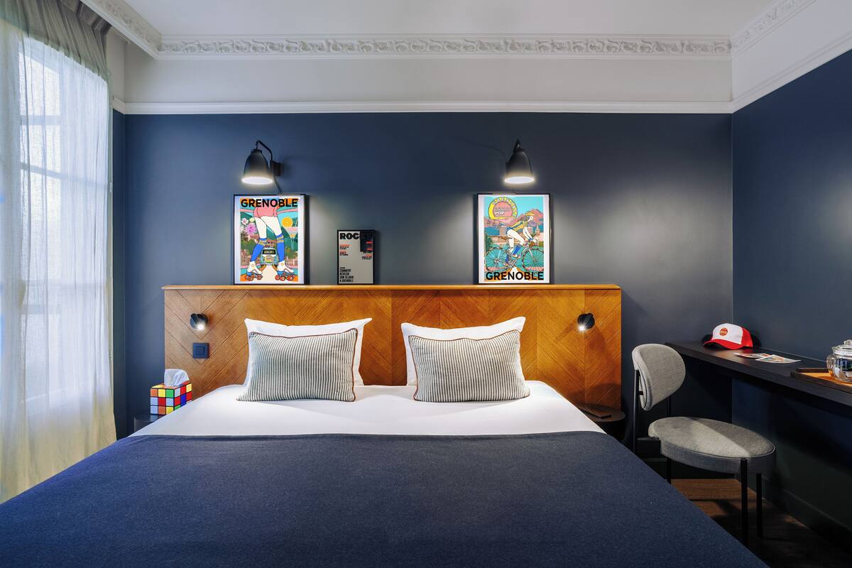 A hotel room with a large bed, two wall-mounted lamps, a wooden headboard, and two posters on the wall.