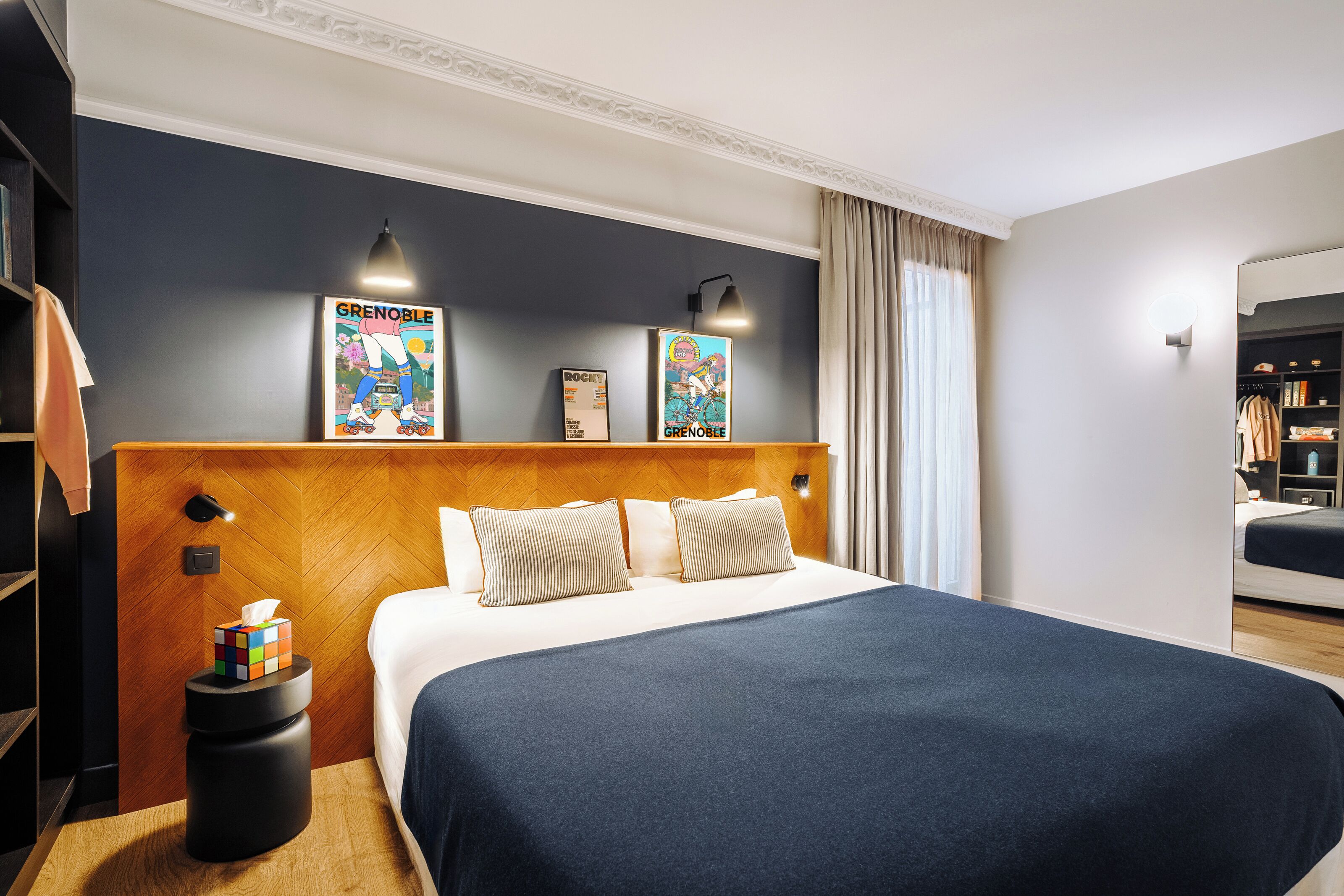 A hotel room with a large bed, a wooden headboard, wall-mounted lights, and a framed poster on the wall.