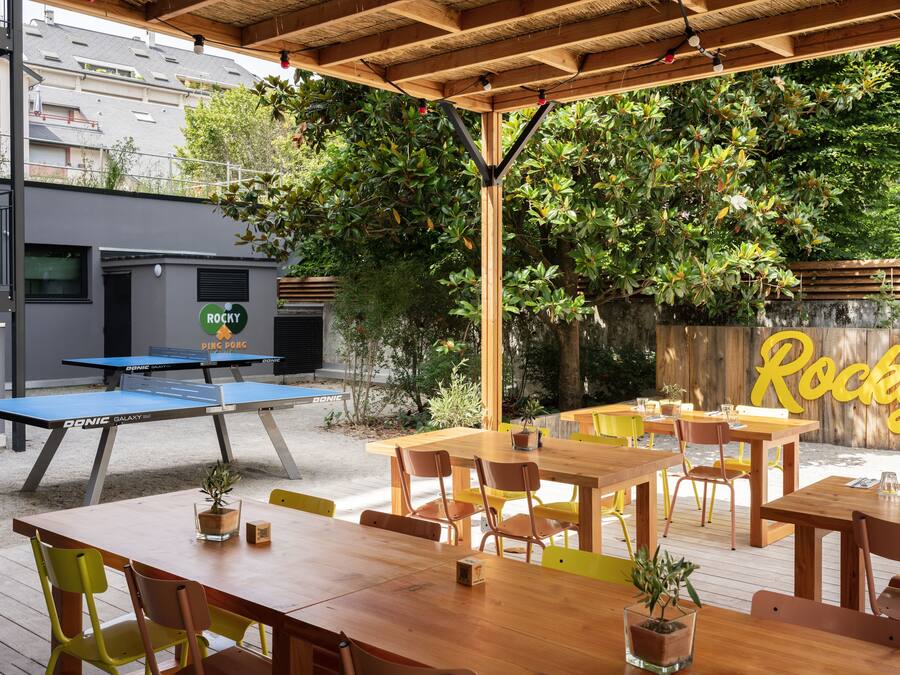 An outdoor patio with wooden tables and chairs, a ping pong table, and a sign that reads "Rocky".