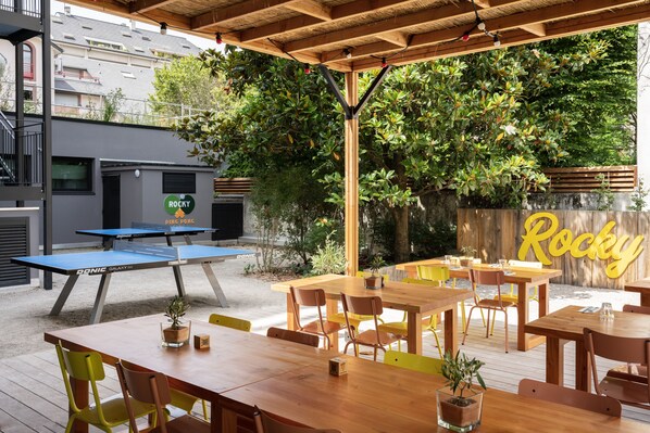 An outdoor patio with wooden tables and chairs, a ping pong table, and a sign that reads "Rocky".