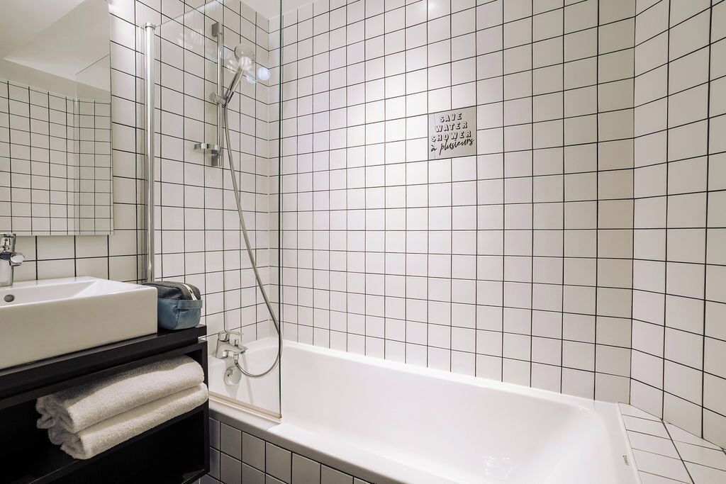 A modern bathroom with a white bathtub, a glass-enclosed shower, and a black vanity with a sink and towels.