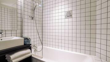 A modern bathroom with a white bathtub, a glass-enclosed shower, and a black vanity with a sink and towels.