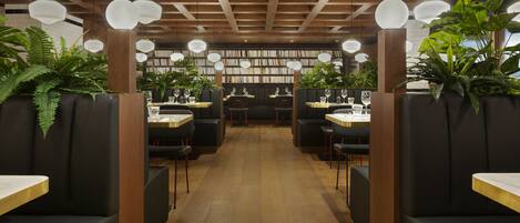 A restaurant with wooden ceiling beams, black cushioned booths, and a central aisle leading to a bookshelf area.