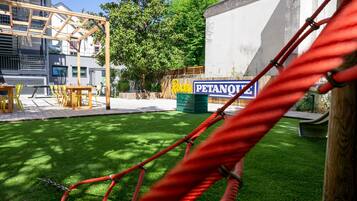 Un parque infantil con un columpio de cuerda, una mesa de picnic y sillas. Se ve un letrero que dice 'Rocky Petanque' al fondo.