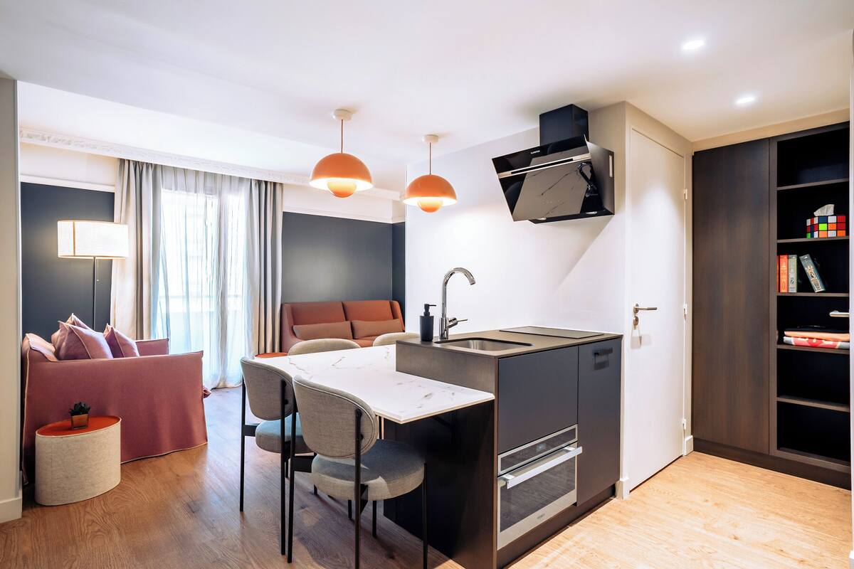 A compact kitchen with a dining area, a sofa, and a bookshelf.