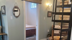 A room with a wooden floor, a chandelier, a bed, and a staircase. - Adorable Downtown Carriage House Cottage (Natchez)