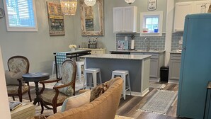 A spacious living area with a large sofa, a dining table, and a kitchen area with a blue refrigerator. - Adorable Downtown Carriage House Cottage (Natchez)