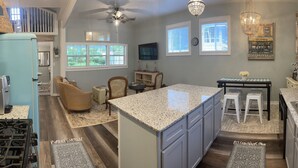 A kitchen with granite countertops, a central island, and a dining area with bar stools. - Adorable Downtown Carriage House Cottage (Natchez)