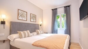 A bedroom with a large bed, two wall-mounted lamps, and two framed palm leaf pictures. - Genteel Home Aire II (Sevilla)