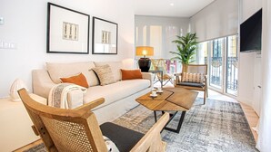 A modern living room with a sofa, coffee table, and chairs. There are framed pictures on the wall, a lamp, and a plant. - Genteel Home Aire II (Sevilla)
