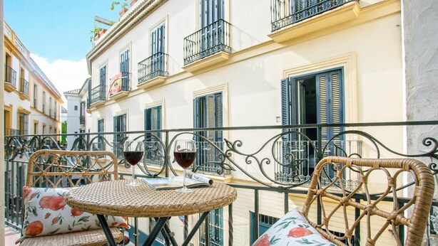 A balcony with wicker furniture, a table, and two wine glasses. - Genteel Home Aire II (Sevilla)