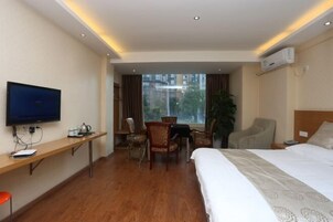 Habitación de hotel con cama, escritorio con televisor, una silla y ventana con vistas a edificios.